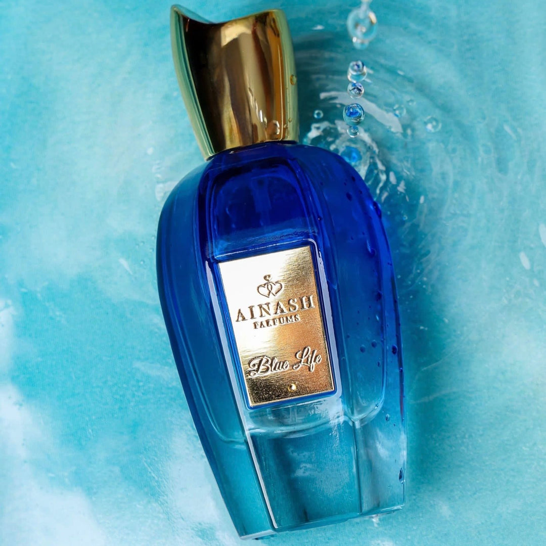 "Blue Life extrait de parfum by Ainash Parfums — royal blue bottle with gold cap and label resting over water-rippled blue background"