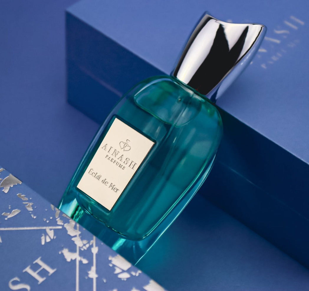 Teal perfume bottle of Éclat de Mer with silver cap placed on luxury blue box with metallic map details