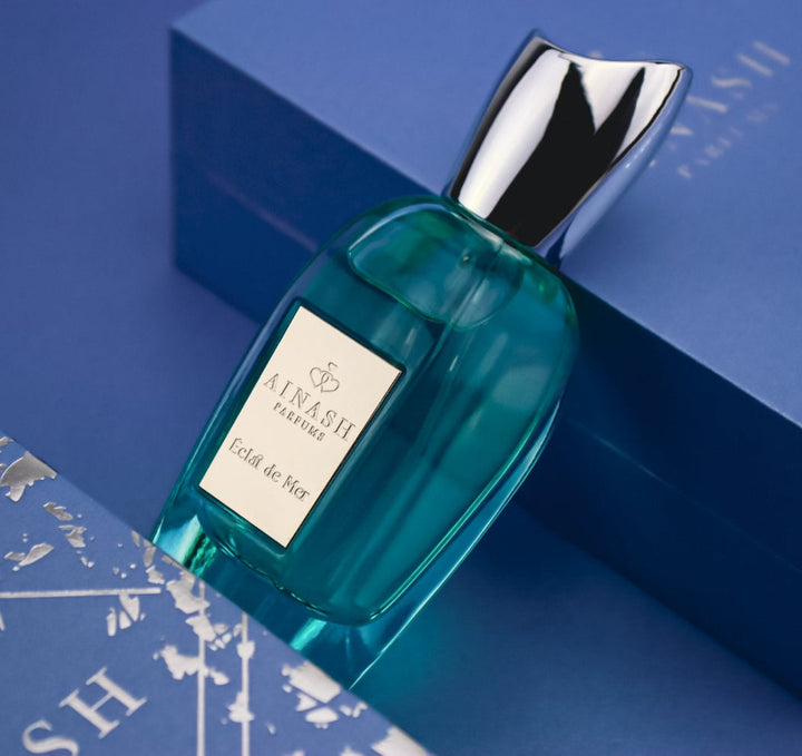 Teal perfume bottle of Éclat de Mer with silver cap placed on luxury blue box with metallic map details