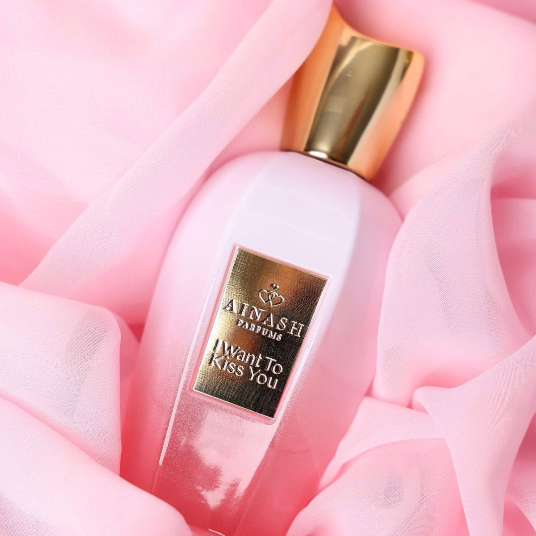 "I Want To Kiss You extrait de parfum by Ainash Parfums — soft pink bottle with gold cap and label nestled in flowing pink fabric"